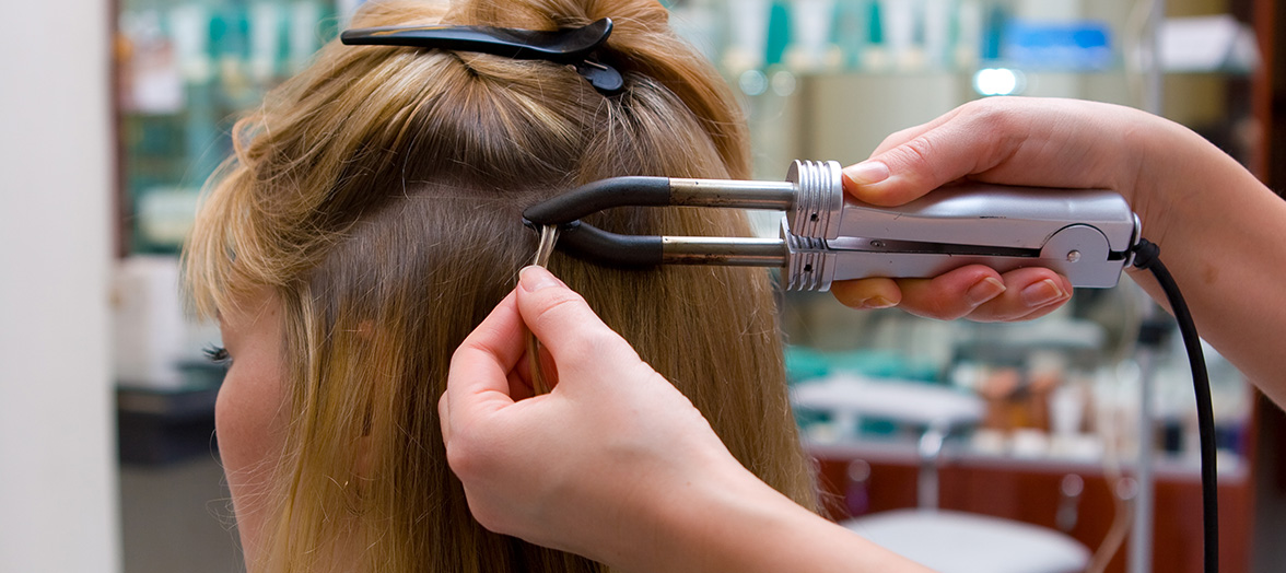 Das Foto zeigt eine Frisörin beim Einarbeiten von Bonding Extensions in das Haar einer Kundin mit einer Wärmezange und einer Schablone