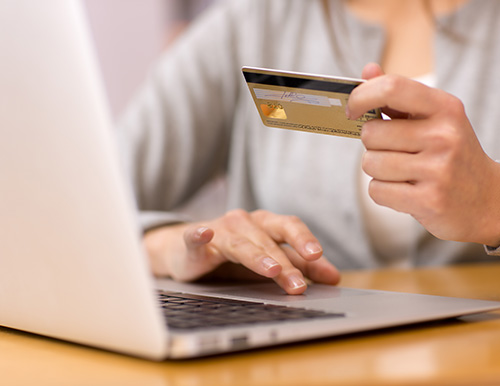 Das Foto zeigt eine Dame vor ihrem Laptop mit einer Kreditkarte in der Hand
